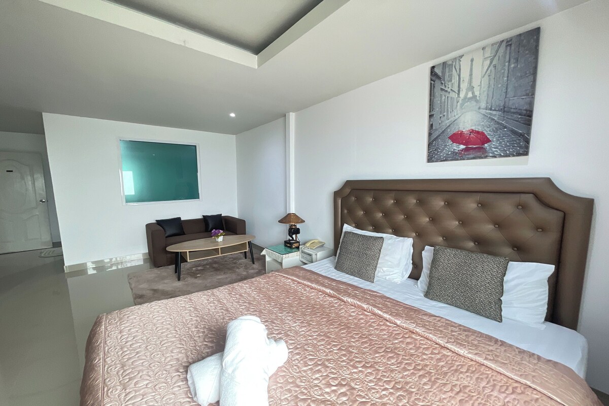 Une chambre d’hôtel avec un grand lit, un canapé, une petite table avec une lampe et un tableau représentant une rue sous la pluie.