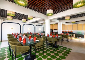 A modern dining area with green chairs, round tables, and a ceiling with hanging lights.