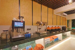 A hotel reception area with a coffee machine, a television, and a buffet counter with orange napkins. - The Orchid Passaros (Benaulim)