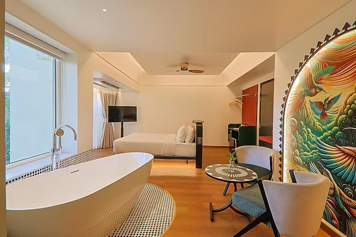 Une chambre d’hôtel moderne dotée d’une grande baignoire, d’un lit, d’une télévision et d’une fresque murale décorative.