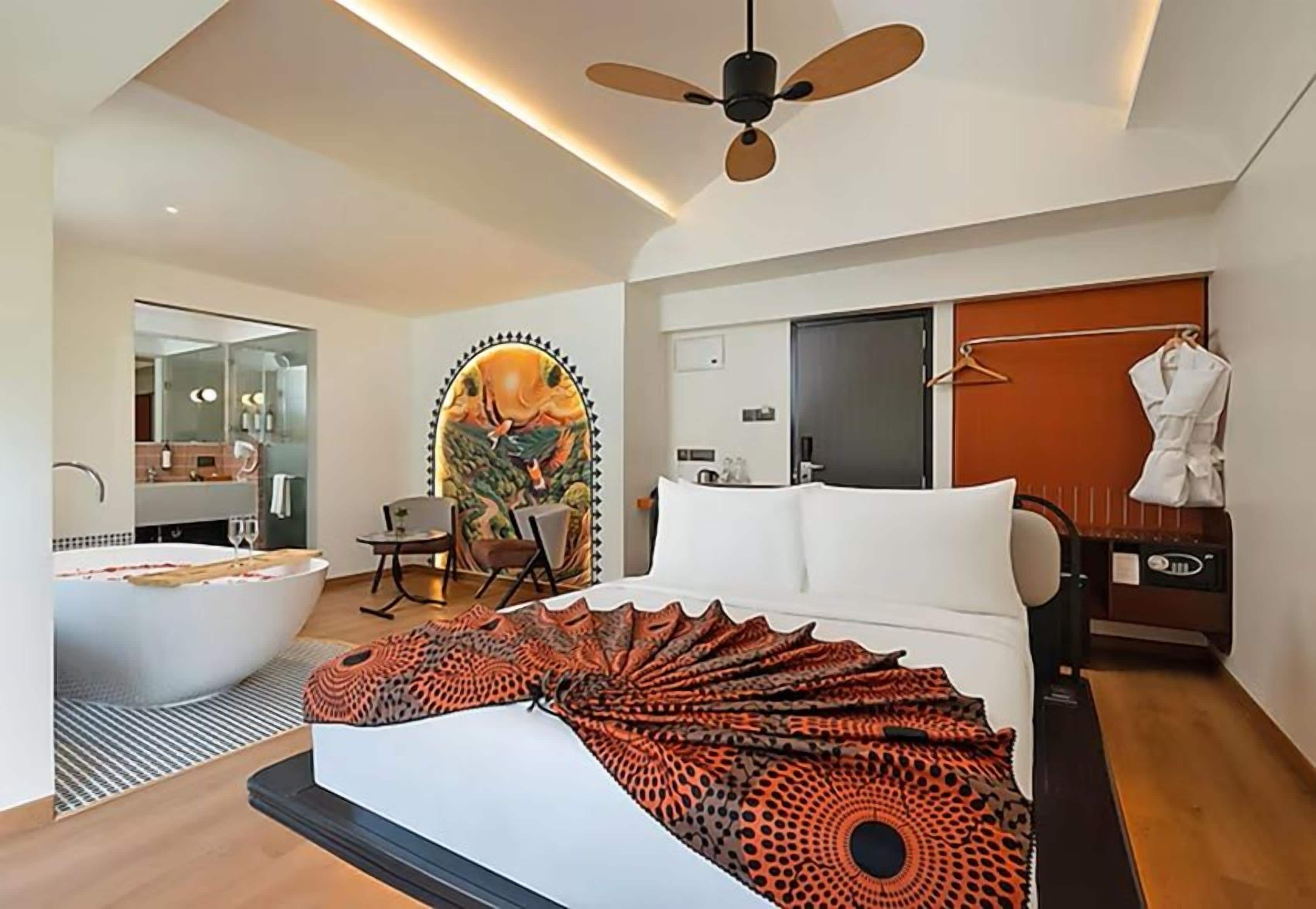 Quarto de hotel moderno com uma cama grande, banheira, ventoinha no teto, guarda-roupa e espelho.