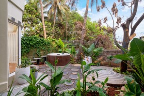 Un giardino tropicale con una vasca idromassaggio, vialetti in pietra e vegetazione lussureggiante.