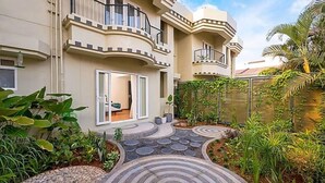 A multi-story residential building with balconies, a paved garden pathway, and surrounding greenery. - The Orchid Passaros (Benaulim)