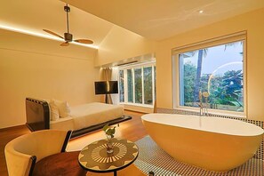 A modern bathroom with a freestanding bathtub, a ceiling fan, and a large window offering a view of greenery. - The Orchid Passaros (Benaulim)