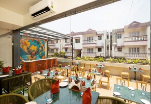 An outdoor dining area with tables and chairs, a colorful mural, and a view of residential buildings.