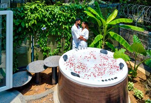 A couple standing by a hot tub with a garden backdrop.