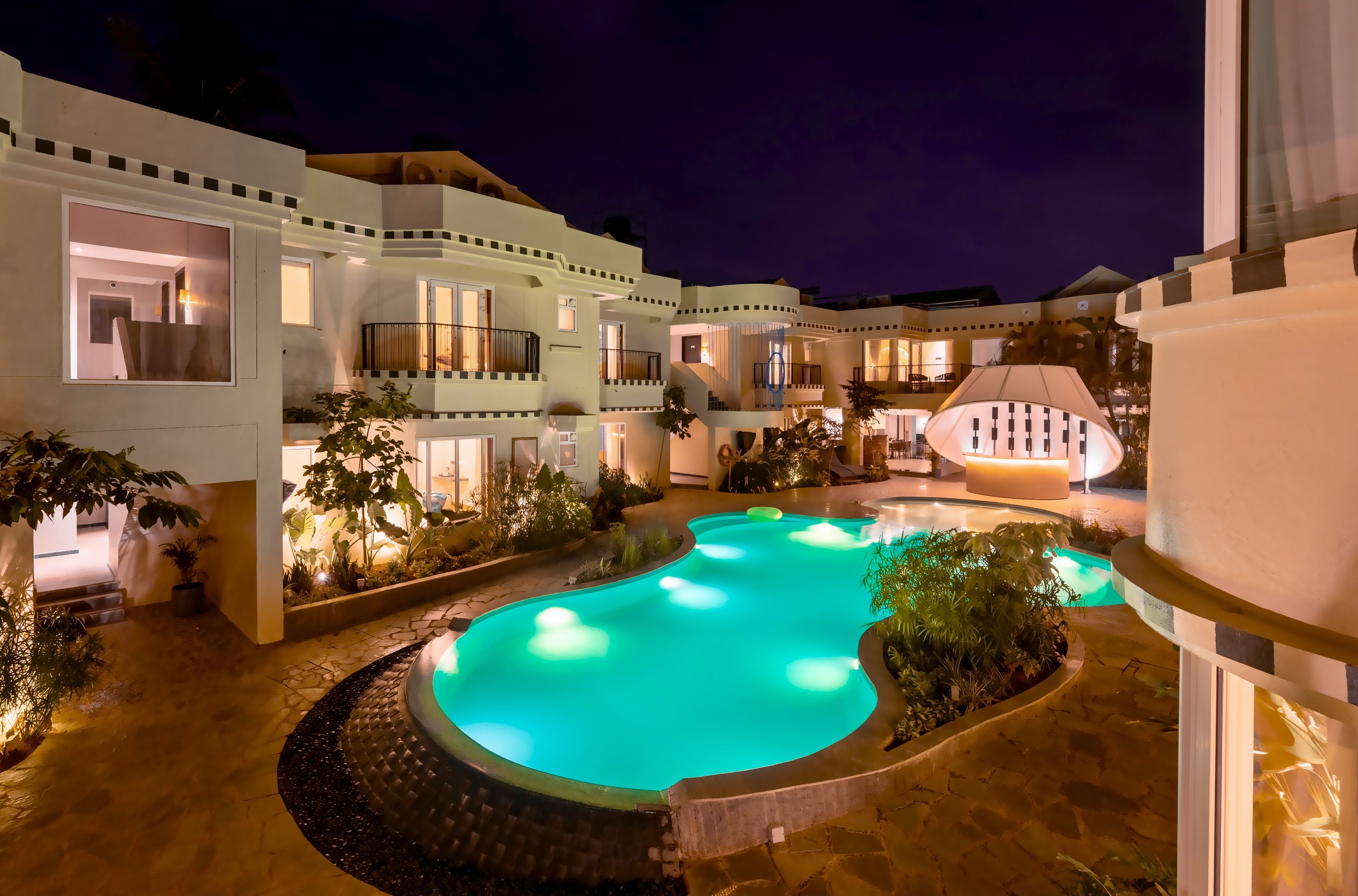 A multi-story hotel with a swimming pool, outdoor lighting, and balconies.