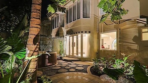 A well-lit outdoor area with a palm tree, a water feature, and a pathway leading to a building with large windows. - The Orchid Passaros (Benaulim)