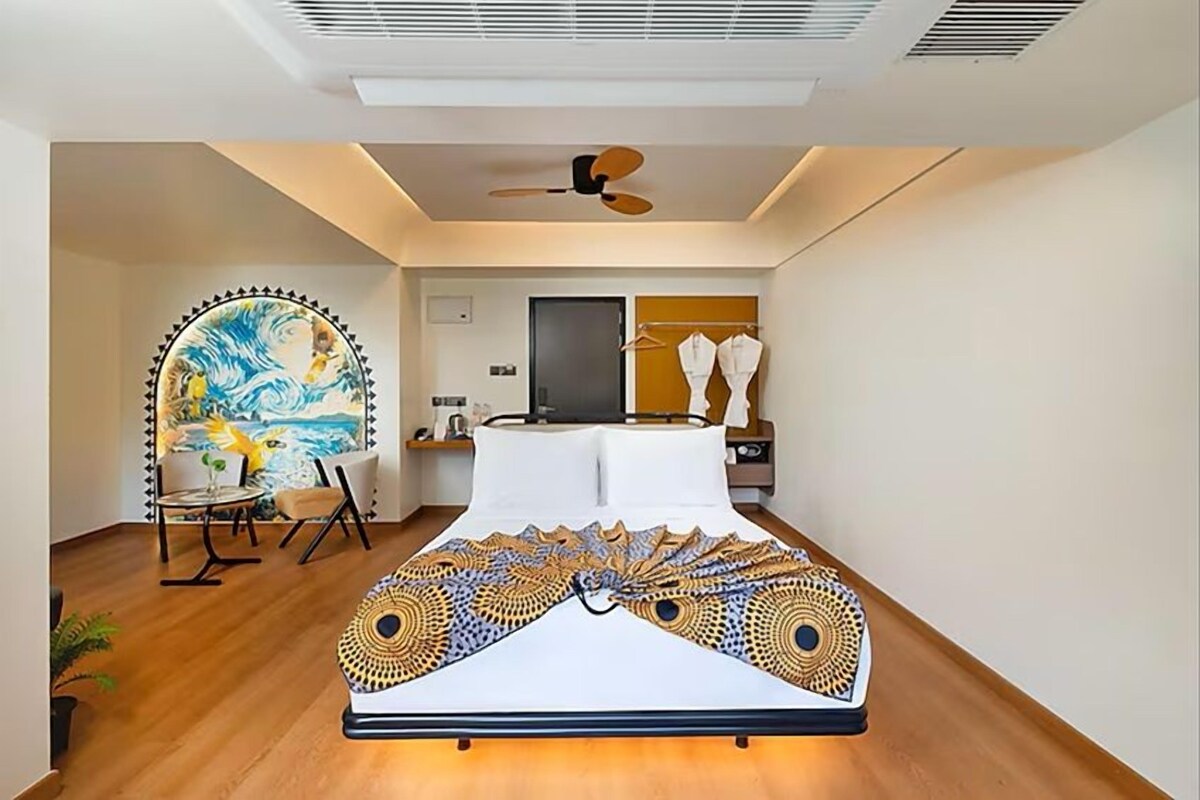 A modern bedroom with a bed, a ceiling fan, a painting, and a chair.
