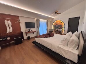 A modern hotel room with a large bed, a flat-screen TV, a ceiling fan, and a window with curtains. - The Orchid Passaros (Benaulim)