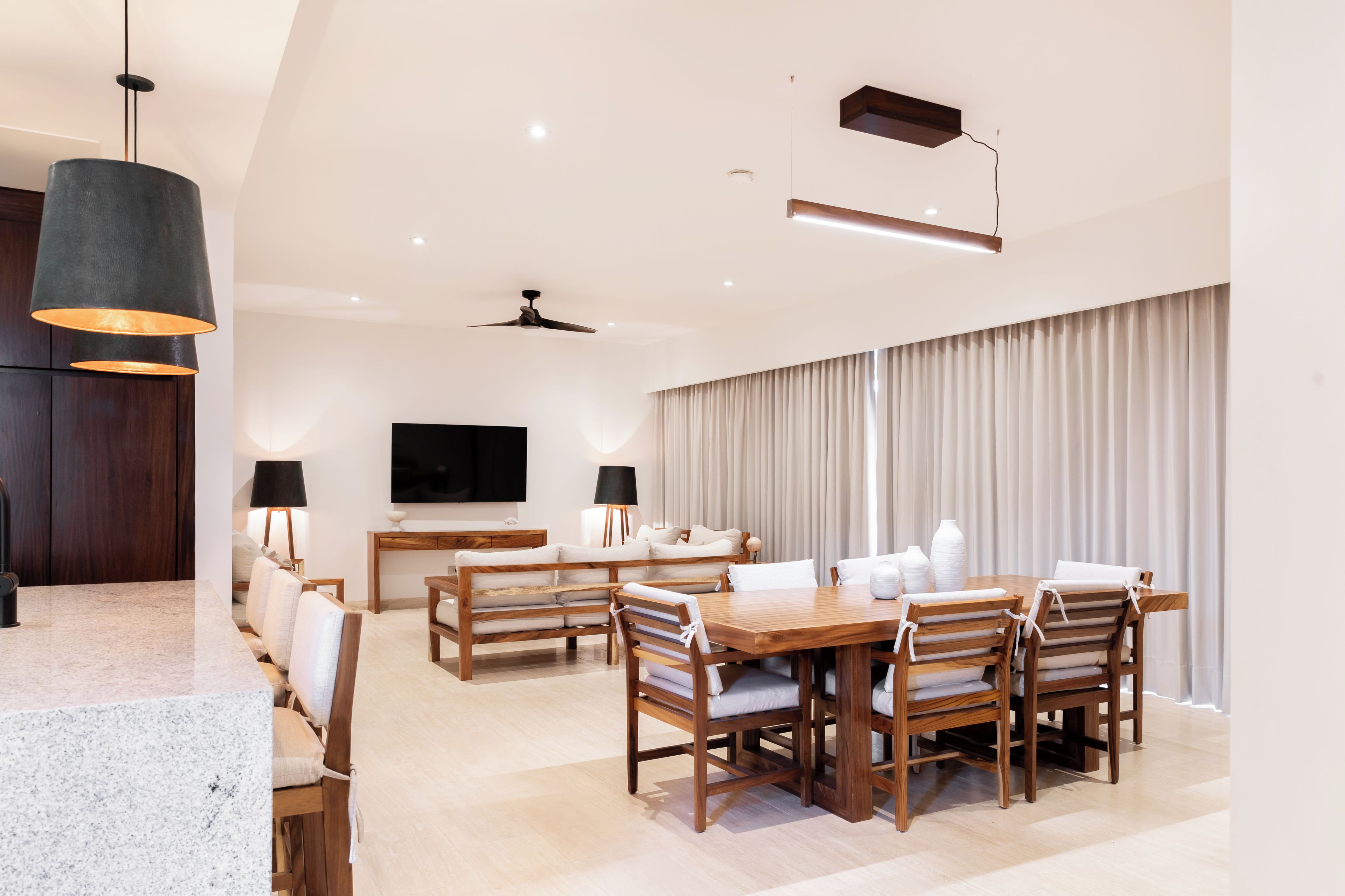 A modern living room with a dining area, wooden furniture, a flat-screen TV, and a ceiling fan.