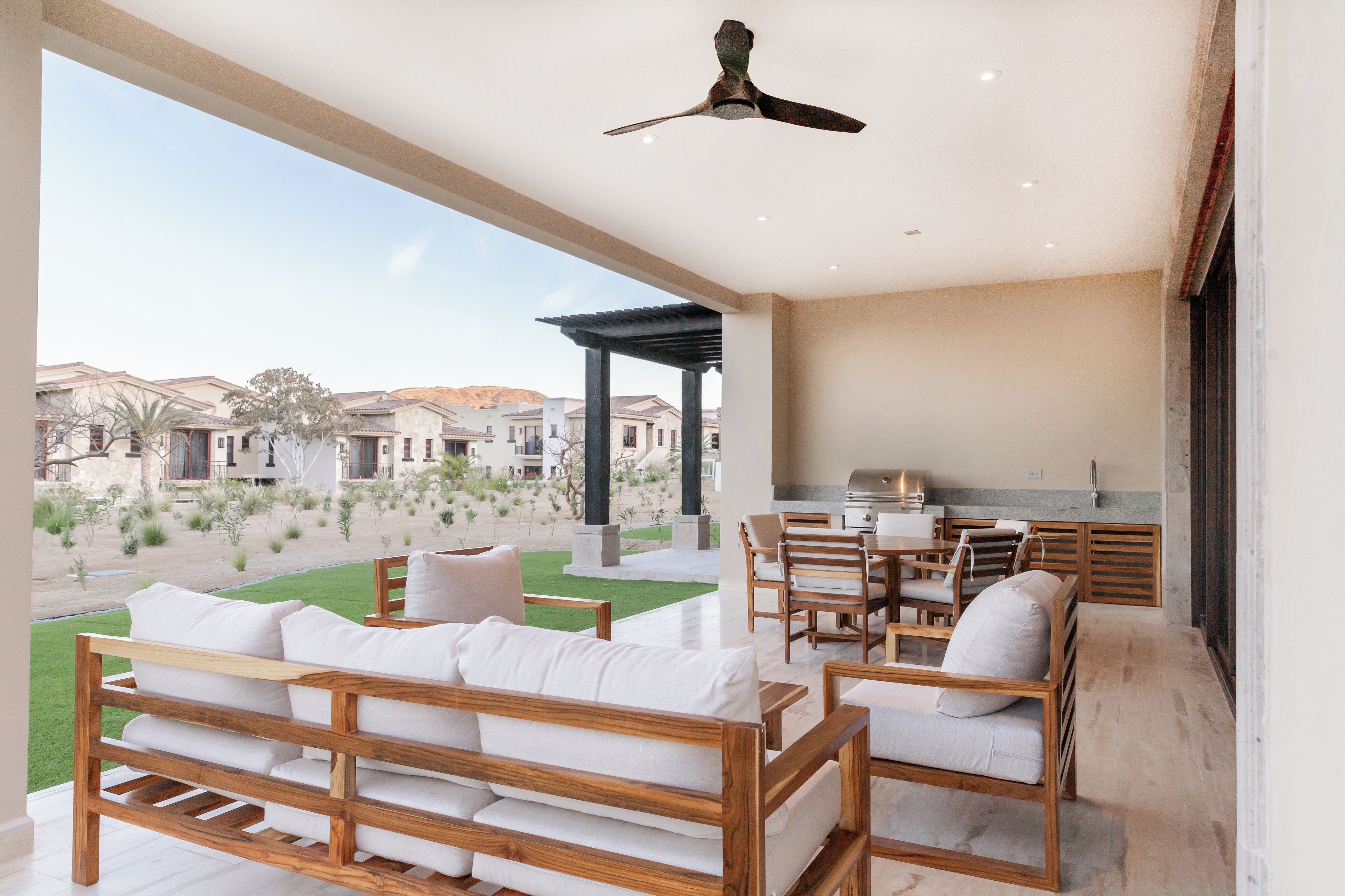 Un patio amplio con un sofá y sillas de madera, una parrilla y vistas a un patio interior con edificios al fondo.