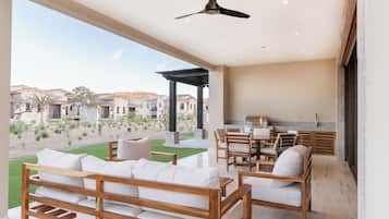 Une vaste terrasse dotée d’un canapé et de fauteuils en bois, d’un barbecue et offrant une vue sur une cour intérieure bordée de bâtiments.