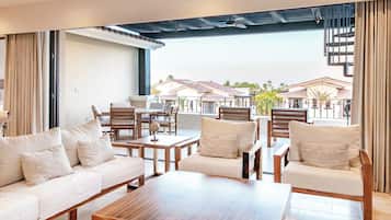 Un espacio lounge moderno con un sofá, sillas y una mesa de centro. Se observa un edificio con tejado de azulejos y palmeras al fondo.