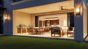 An outdoor dining area with wooden furniture and a grill, connected to a kitchen with modern appliances. - Bohari (San José del Cabo)