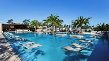 Una piscina grande y transparente con sillas de descanso y palmeras.