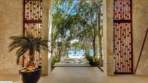 A stone-walled corridor leading to a pool area with a view of trees and a clear sky. - Bohari (San José del Cabo)