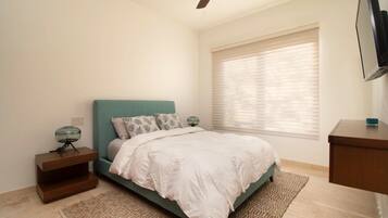 Ein Schlafzimmer mit Bett, Nachttischen, Deckenventilator, einem Fenster mit Jalousien und einem Fernseher auf einem Schrank.