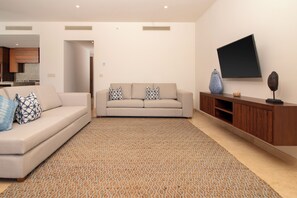 A modern living room with a beige sofa, patterned rug, and a flat-screen TV mounted on the wall. - Bohari (San José del Cabo)