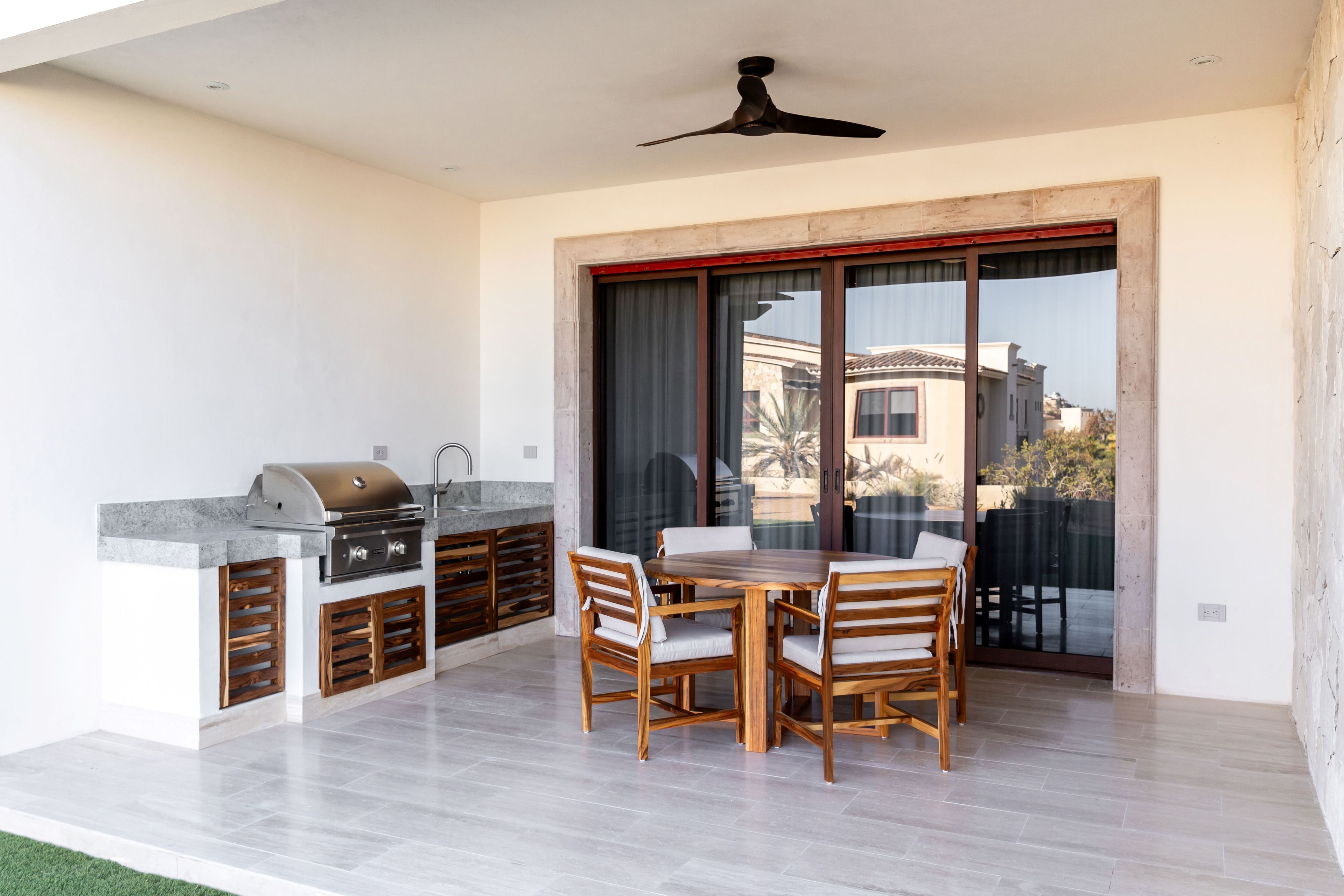 An outdoor patio with a barbecue grill, wooden dining table, and chairs.