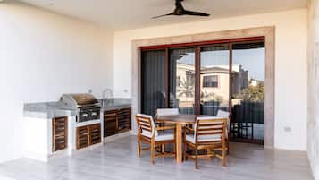 Un patio al aire libre con una parrilla, una mesa de comedor de madera y sillas.