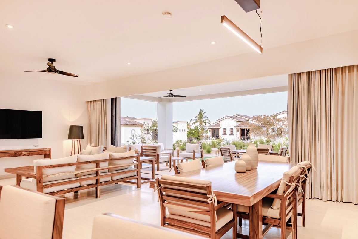 A spacious living area with a large wooden table and chairs, a TV, and a ceiling fan.