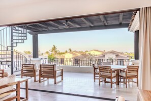 A spacious balcony with wooden furniture, a spiral staircase, and a view of houses in the background. - Bohari (San José del Cabo)