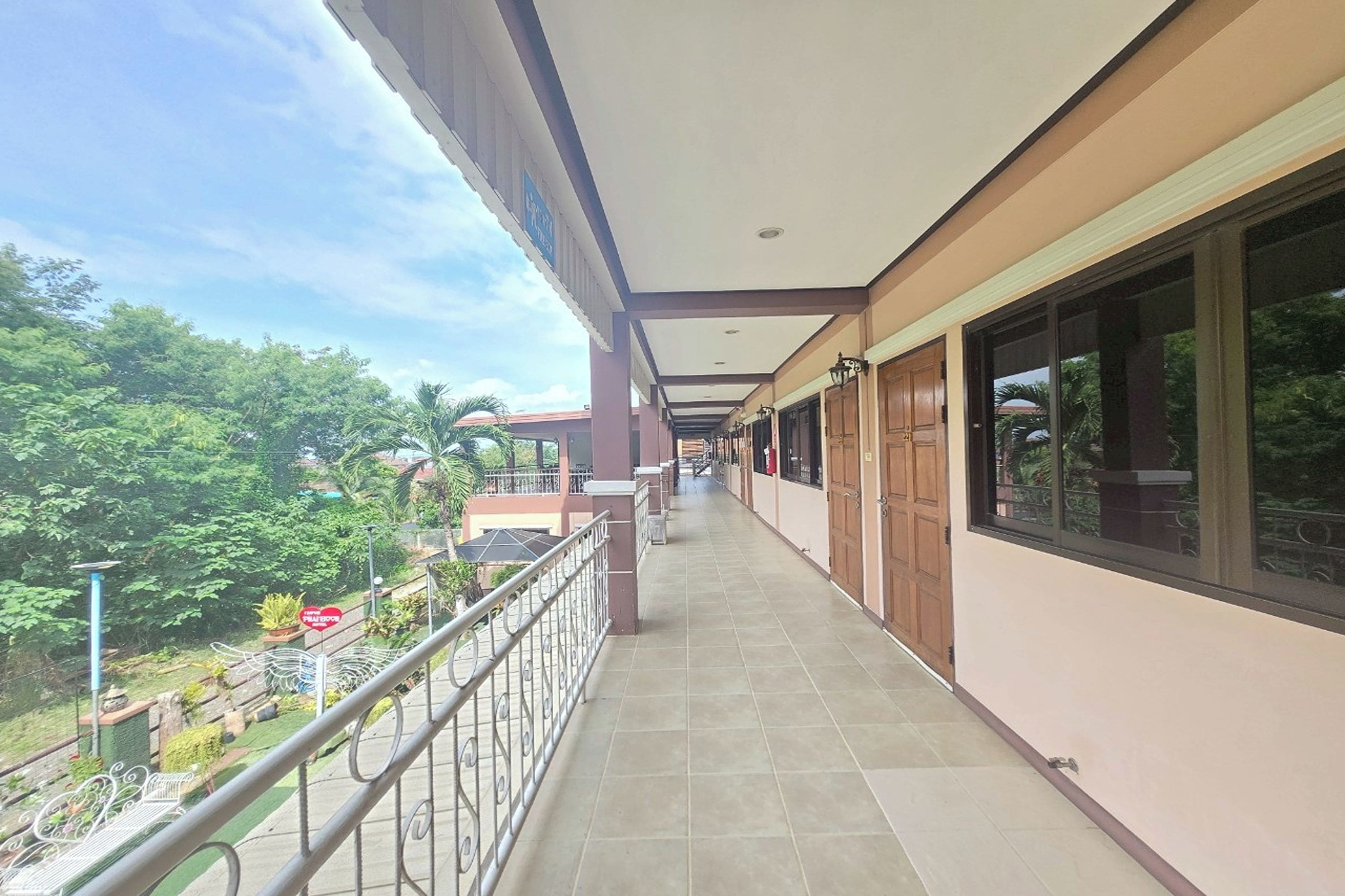 A long, covered corridor with a metal railing, leading to a building with large windows and doors.