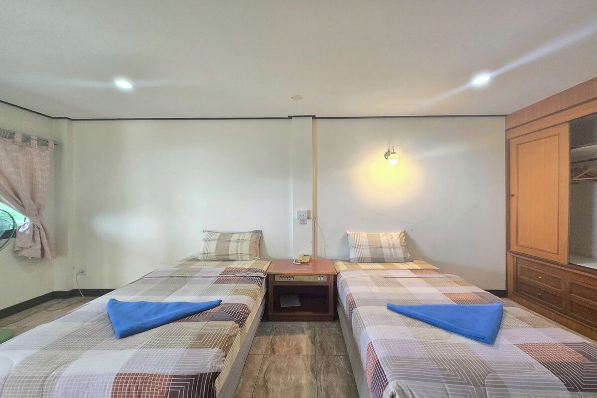Een kamer met twee bedden, een houten nachtkastje, een wandlamp en een kledingkast.
