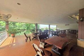 A spacious outdoor dining area with wooden tables and chairs, potted plants, and ceiling fans. - Phaiboon Hotel & Resort By Zuzu (Pak Chong)
