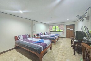 Habitación de hotel con cuatro camas, televisión, escritorio y ventilador.
