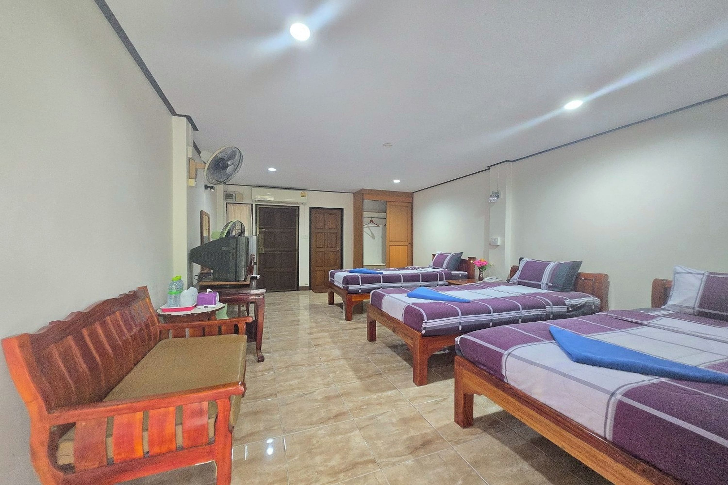 A hotel room with two beds, a wooden chair, a small table, a TV, and a fan.