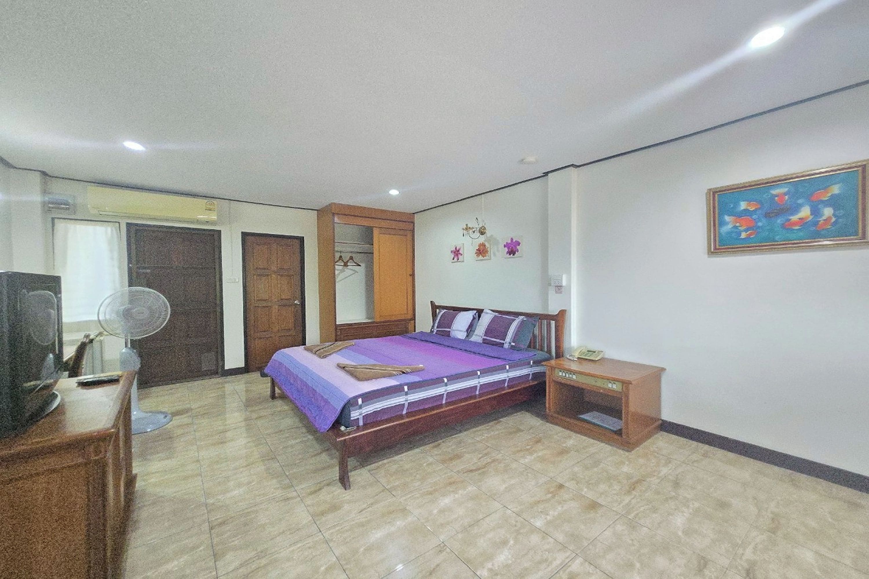 Quarto com cama, mesa de cabeceira, televisão, ventoinha e guarda-roupa.