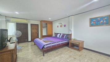 Quarto com cama, mesa de cabeceira, televisão, ventoinha e guarda-roupa.