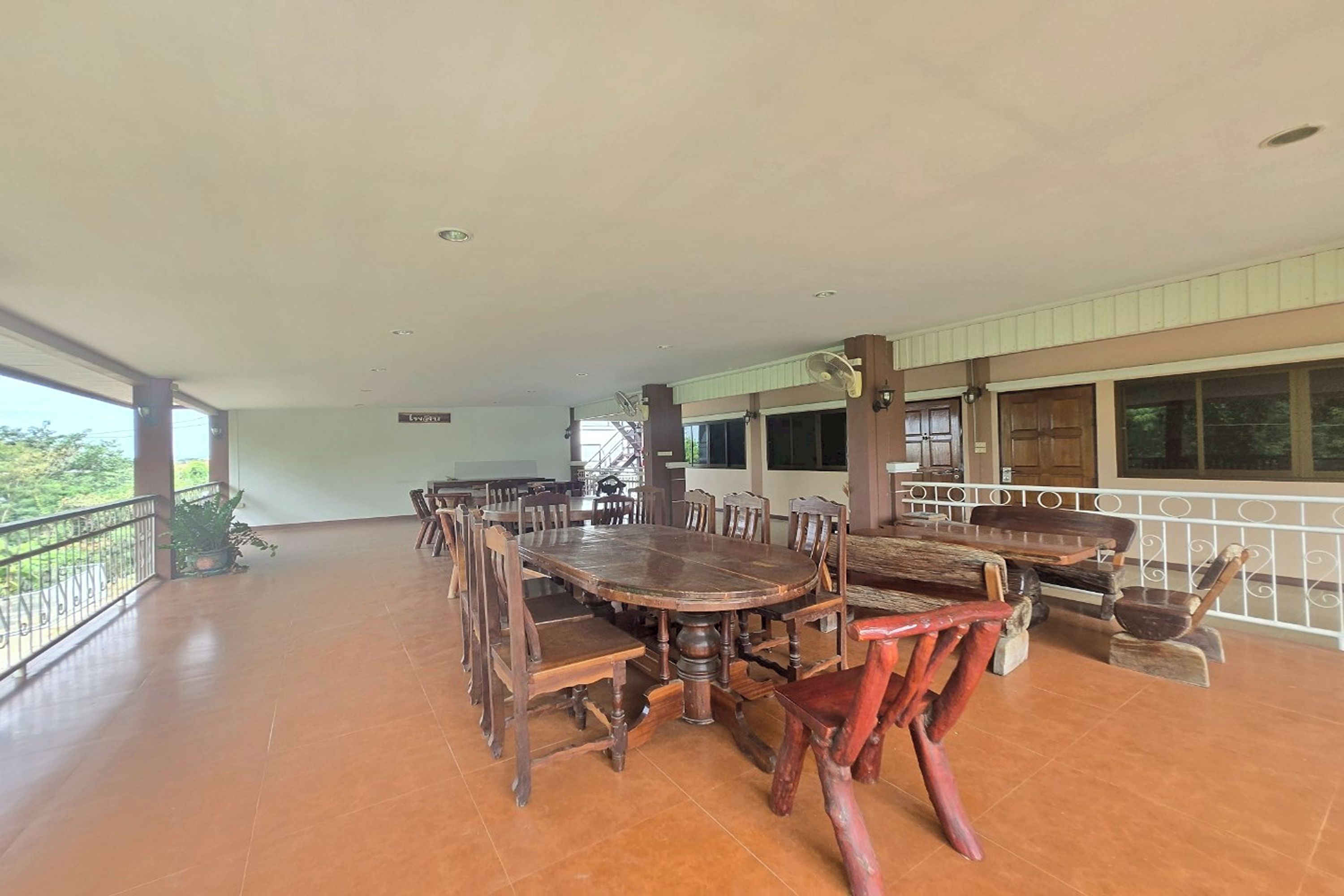 A spacious dining area with a large wooden table and chairs, a balcony with a railing, and a view of the outdoors.