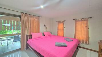 Quarto com uma cama grande, duas janelas com cortinas, uma varanda com uma cadeira e vista para áreas verdes.