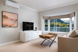 Un salon moderne doté d’un téléviseur à écran plat, d’une machine à café et offrant une vue sur un balcon avec une chaîne de montagnes en arrière-plan.