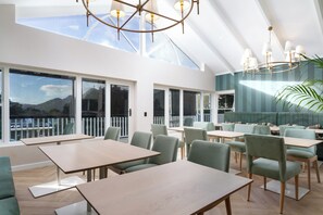 Un espace de restauration moderne, doté de tables et de chaises, de grandes fenêtres et offrant une vue sur l’extérieur.