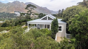 A house with a covered porch, surrounded by dense greenery and mountains in the background. - Bay Haven Collection, Hout Bay (Cape Town)