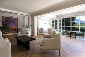 A spacious living room with a large window, a painting, and a coffee table. - Bay Haven Collection, Hout Bay (Cape Town)