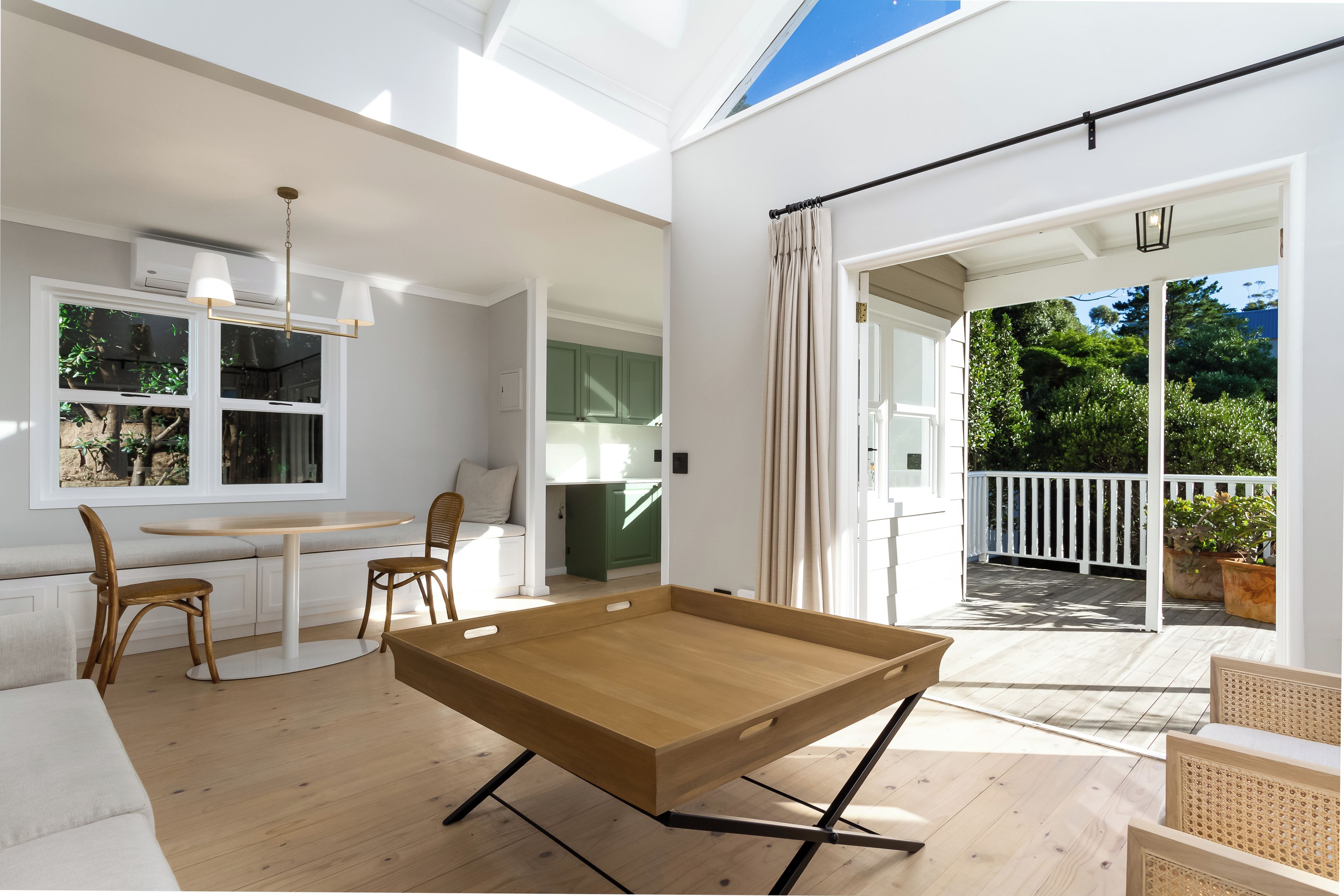 A spacious room with a wooden table, a sofa, and a view of a balcony with a white railing.