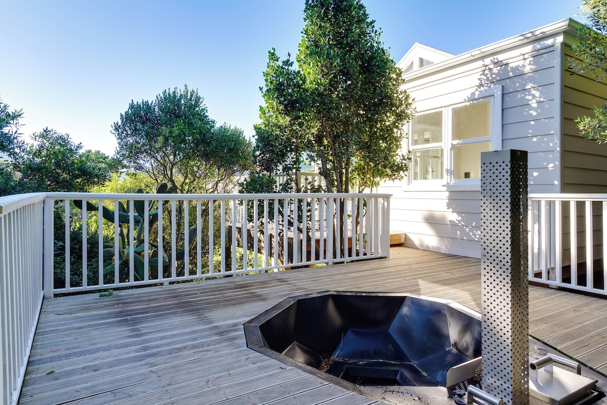 A wooden deck with a hot tub, a white railing, and a house in the background.