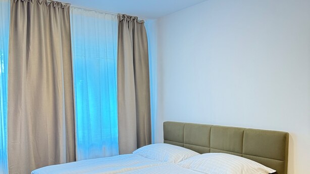 A single bed with a green headboard in a room with wooden flooring and light-colored walls. - Riverside Apartment (Prague)