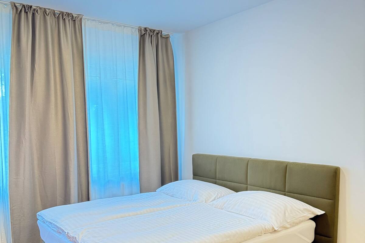 A single bed with a green upholstered headboard in a room with wooden flooring and light-colored walls.