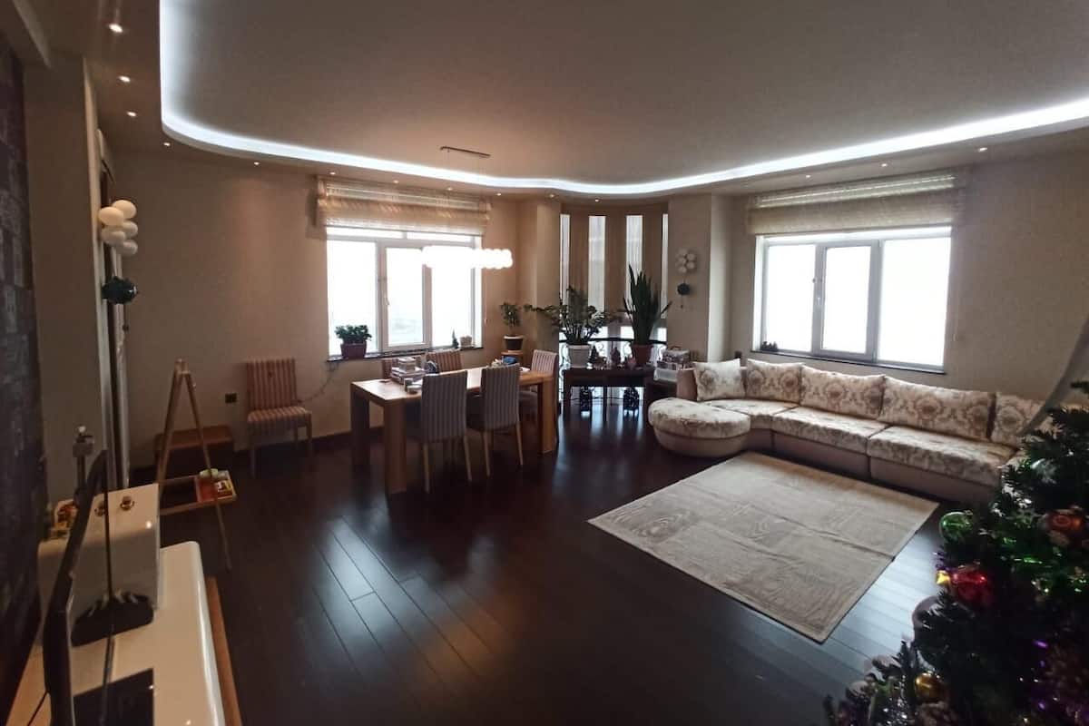 A modern living room with a large sectional sofa, a dining area with a table and chairs, and a Christmas tree.