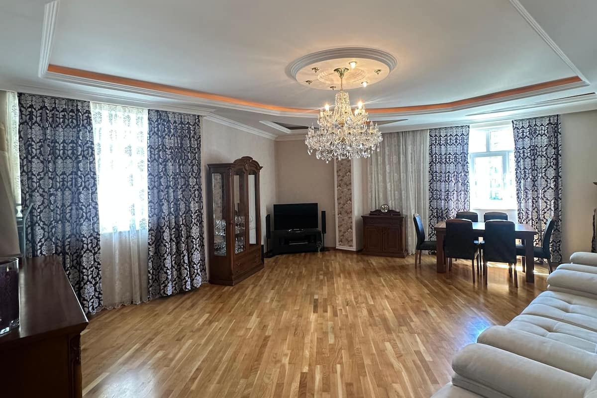 A spacious living room with a wooden floor, a chandelier, a sofa, a TV, and a dining area.