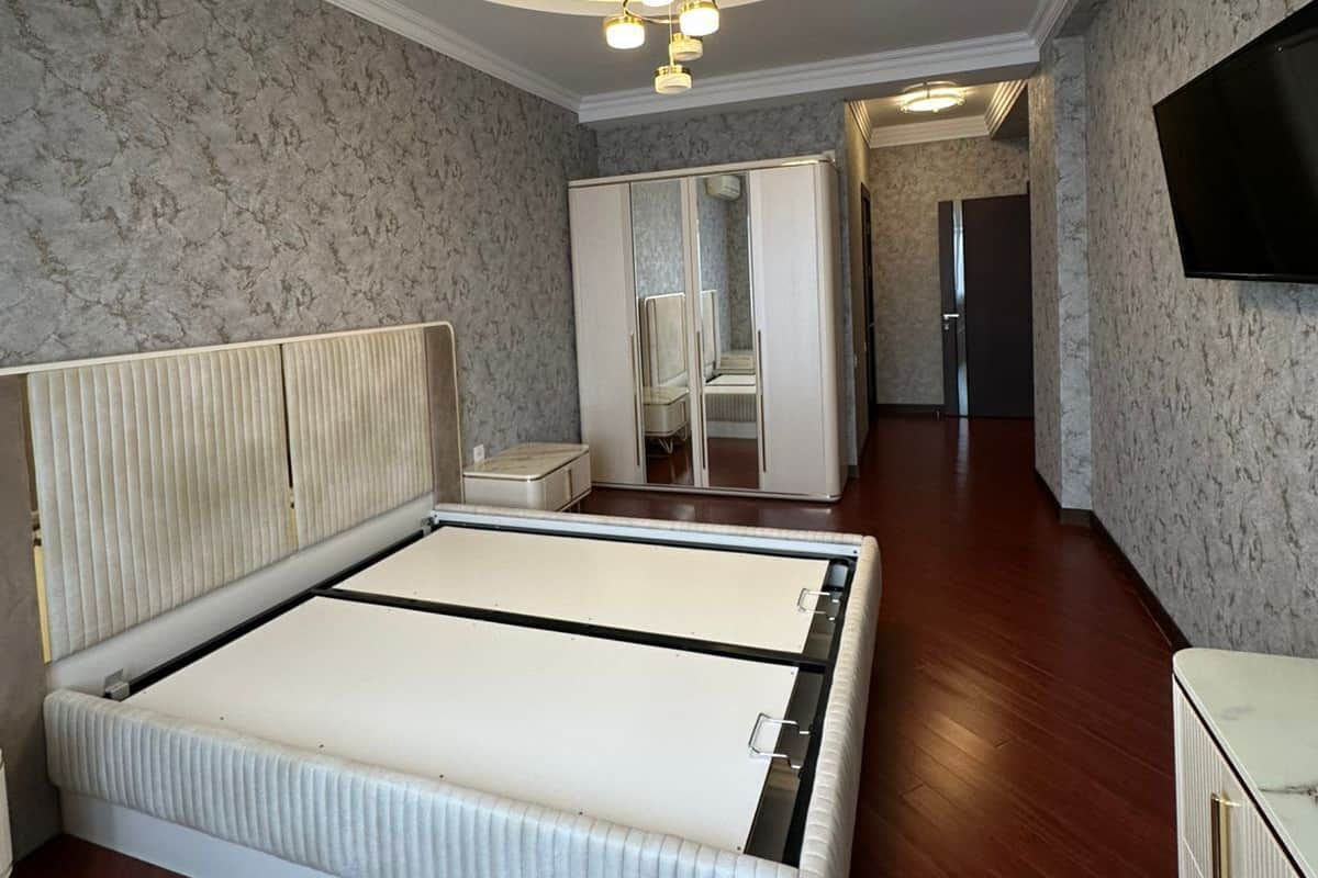 A bedroom with a large bed, a wardrobe, a mirror, and a TV on the wall.