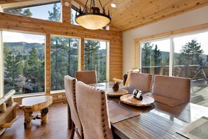 A wooden interior with large windows, a dining table, and chairs. - Silver Tip Chalet #2141 (Big Bear Lake)