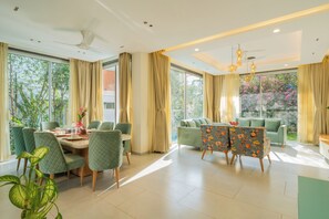 A spacious dining area with a table set for four, surrounded by green upholstered chairs. - Elivaas Laguna Aurelia - Goa (Vagator)