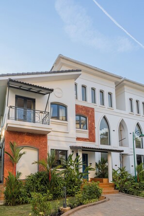 A two-story house with a balcony, a red brick section, and a well-maintained garden. - Elivaas Laguna Aurelia - Goa (Vagator)